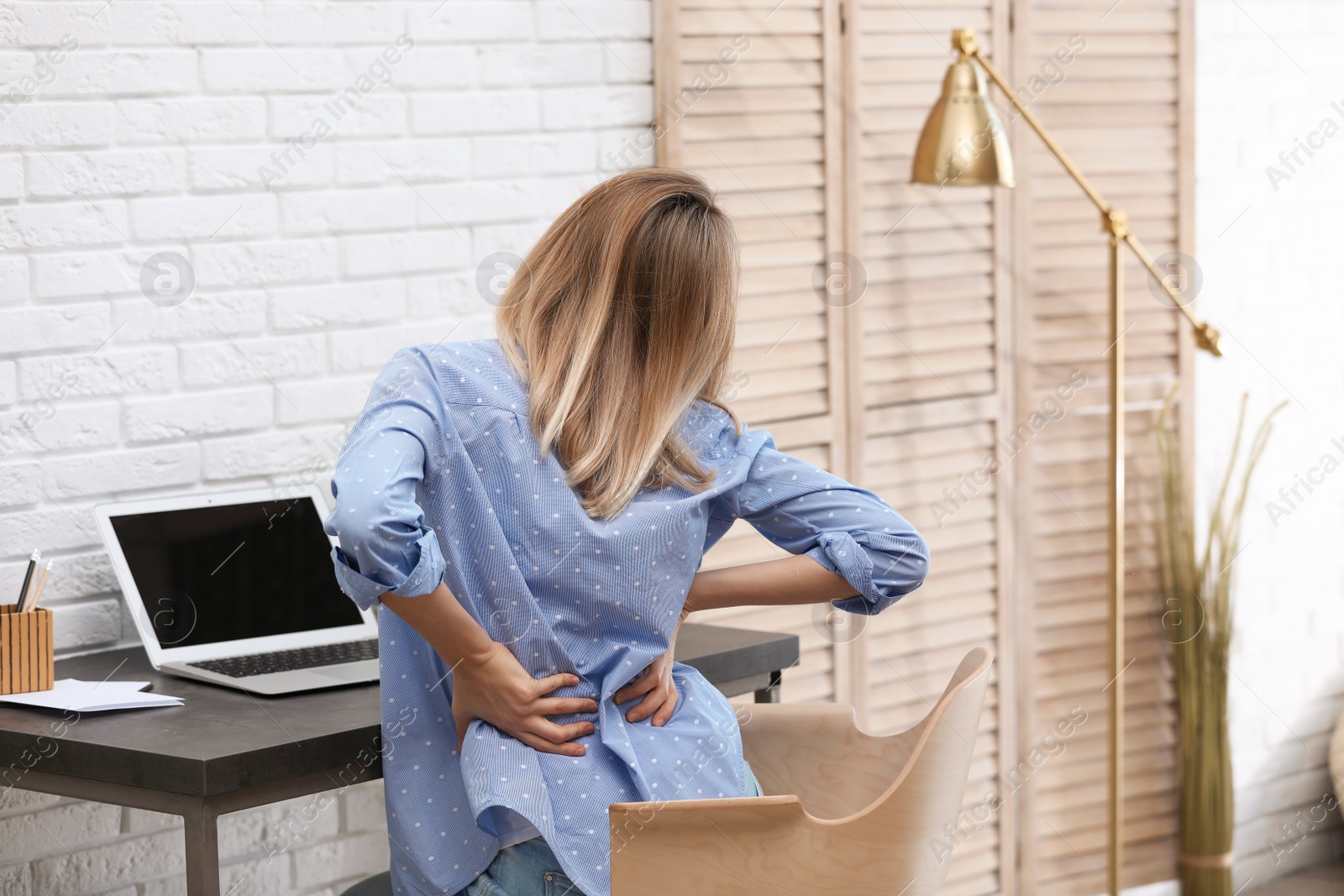 Photo of Young woman suffering from back pain in office