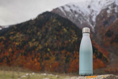 Thermo bottle on rock in mountains. Space for text