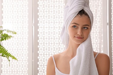 Photo of Beautiful teenage girl wiping face with towel near mirror at home, space for text
