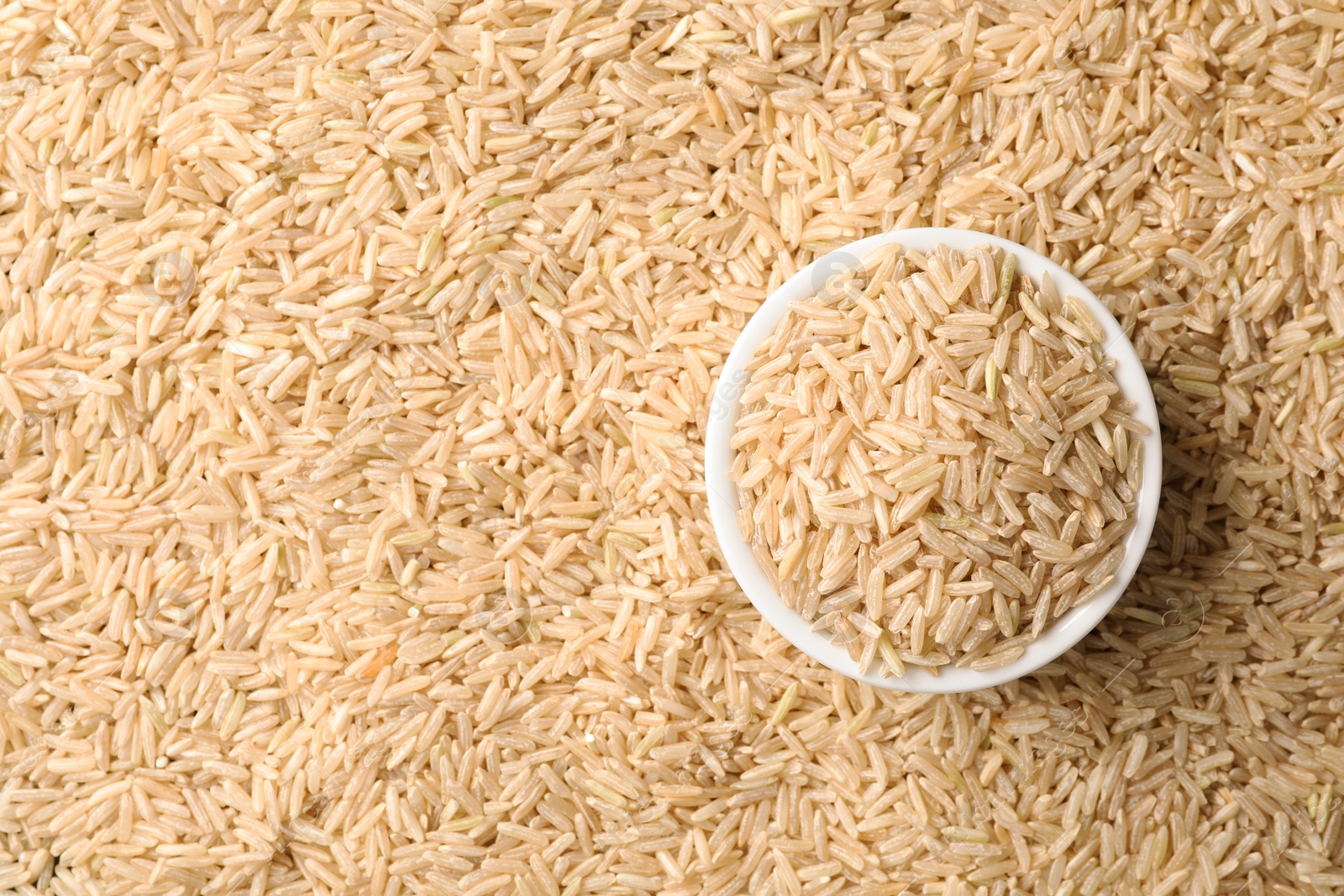 Photo of Ceramic bowl with cereal on raw brown rice, top view. Space for text