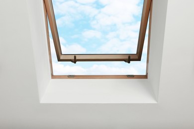 Open skylight roof window on slanted ceiling in attic room, bottom view