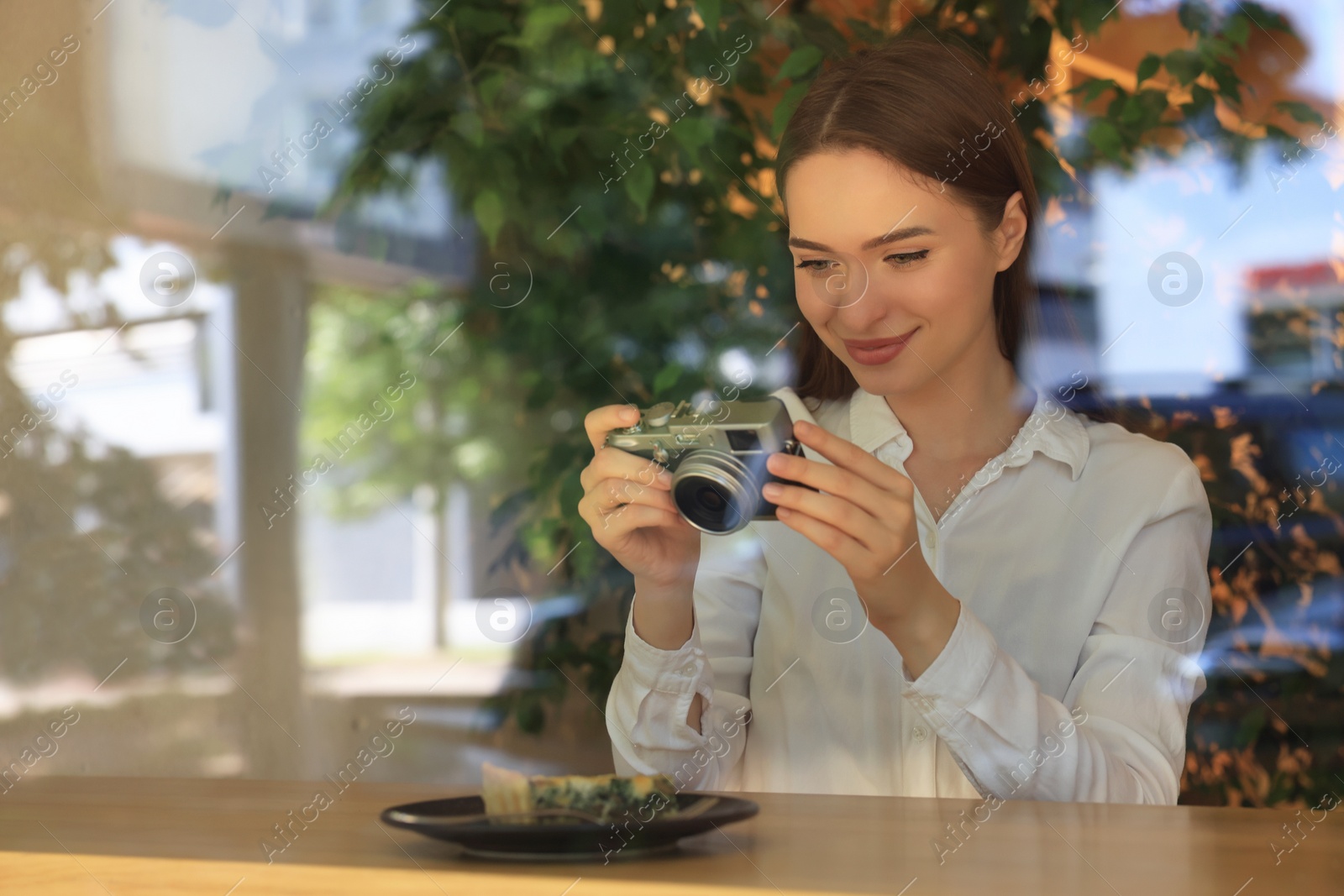 Photo of Young woman taking photo of plate with pie at cafe, view through window. Creative hobby