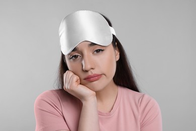 Photo of Tired young woman with sleep mask on light grey background. Insomnia problem