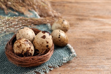 Photo of Nest and quail eggs on wooden table. Space for text