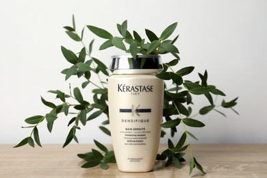 Photo of MYKOLAIV, UKRAINE - SEPTEMBER 07, 2021: Kerastase shampoo and green branches on wooden table. Hair care cosmetic product