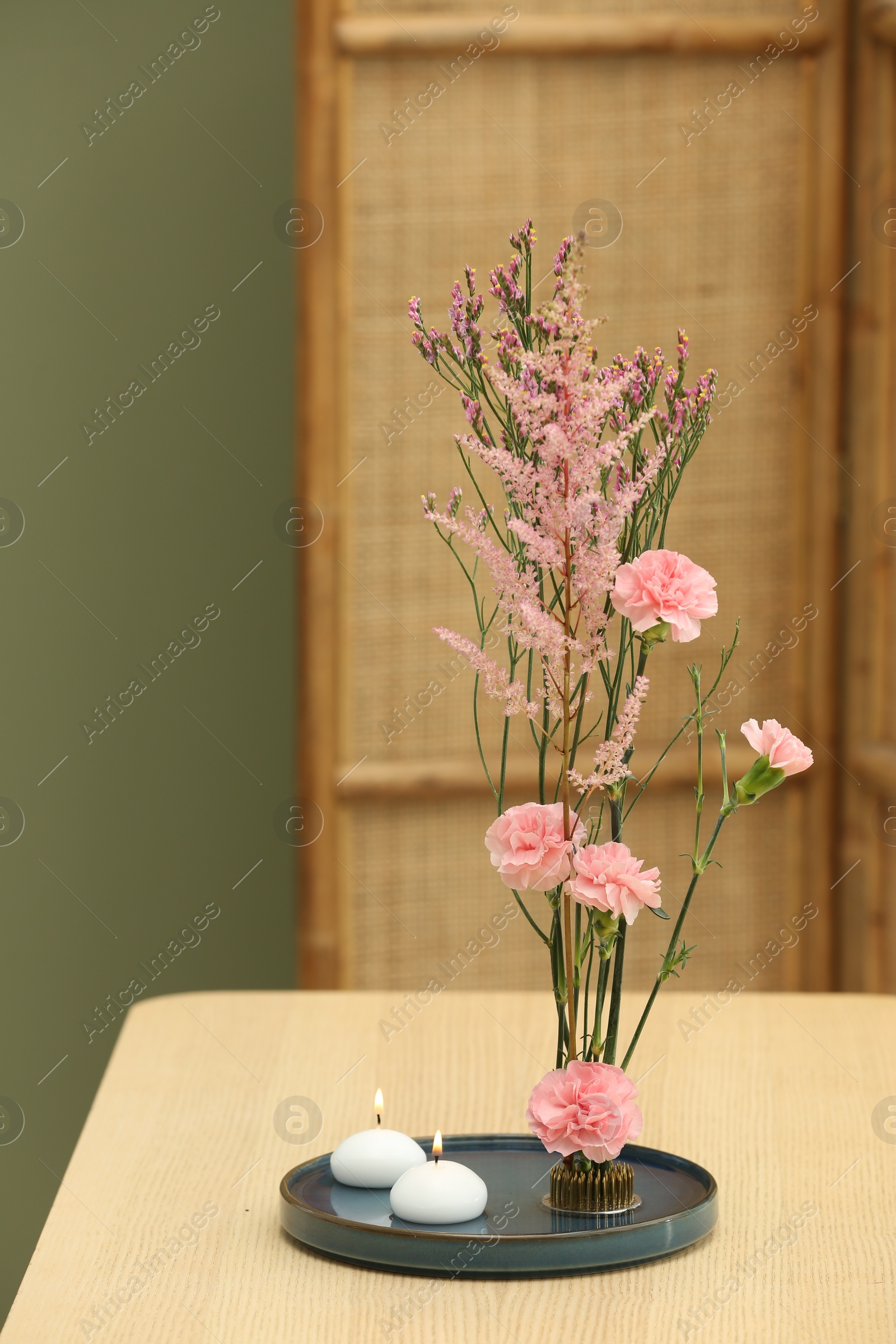 Photo of Stylish ikebana with beautiful pink flowers and burning scented candles carrying cozy atmosphere at home