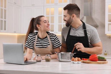 Happy lovely couple using laptop while cooking in kitchen