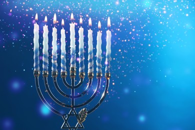 Image of Hanukkah celebration. Menorah with burning candles on blue background, closeup. Space for text
