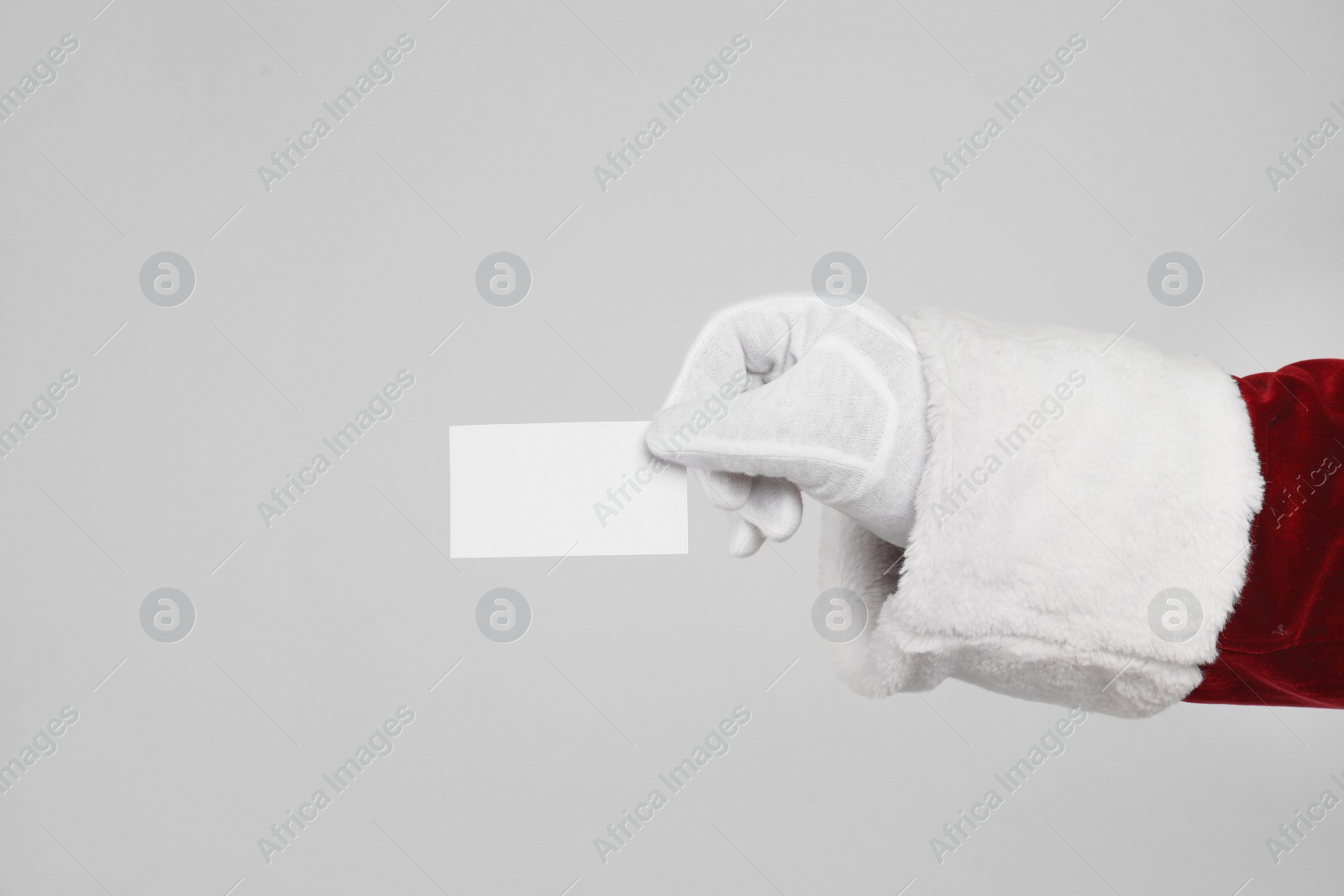 Photo of Santa Claus holding blank card on light grey background, closeup of hand. Space for text