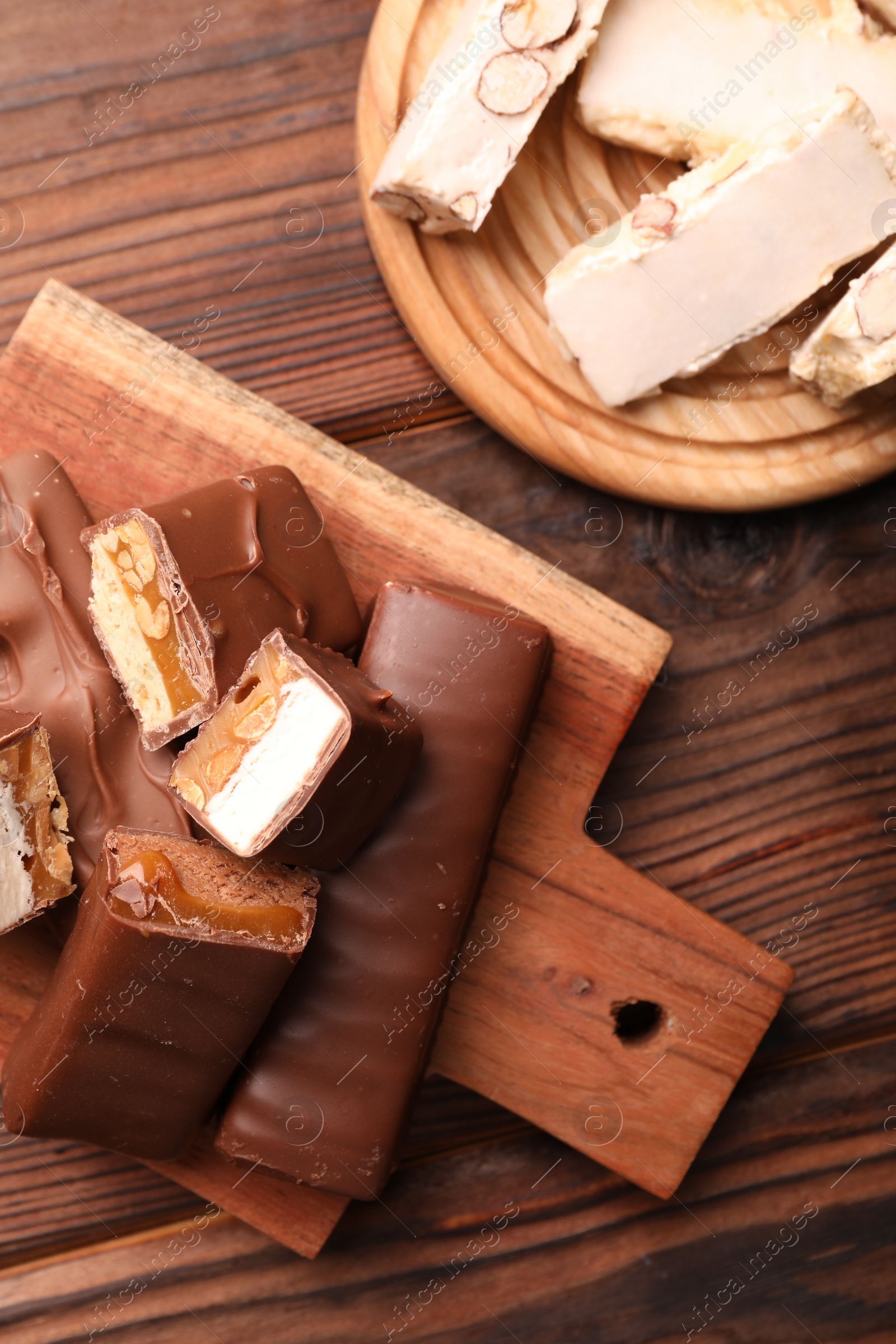 Photo of Tasty chocolate bars and nougat on wooden table, flat lay