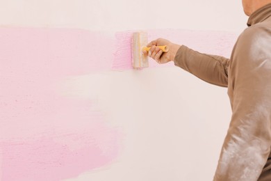 Decorator painting wall indoors, closeup. Space for text