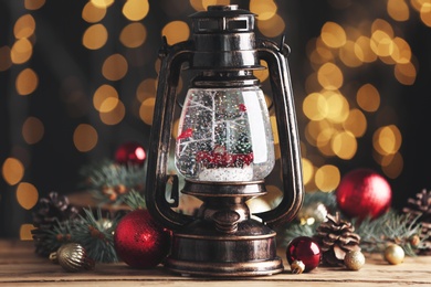 Beautiful snow globe in vintage lantern and Christmas decor on wooden table against blurred festive lights