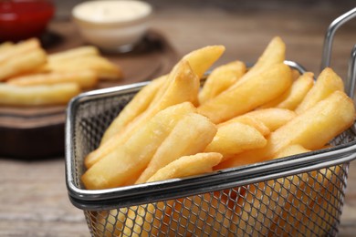 Photo of Tasty French fries in metal basket on table, closeup