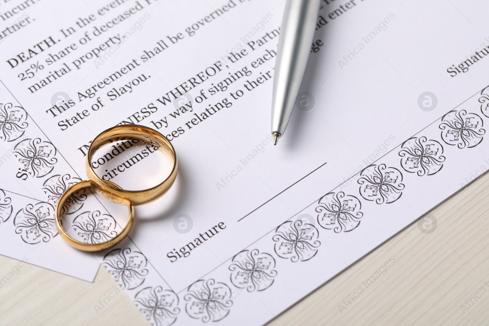 Photo of Marriage contract, gold rings and pen on light wooden table, closeup