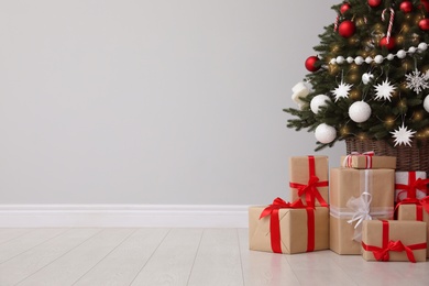 Photo of Gift boxes under decorated Christmas tree near grey wall. Space for text