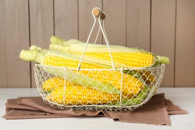 Photo of Tasty fresh corn cobs in metal basket on white wooden table