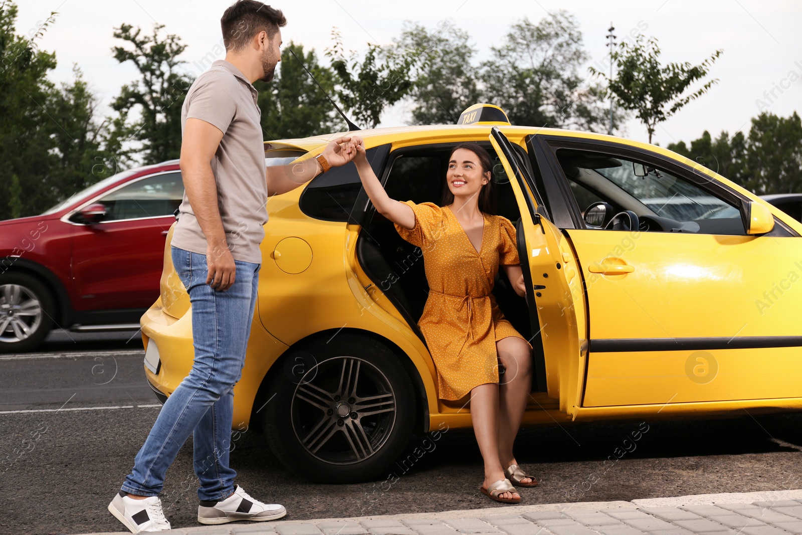 Photo of Man helping young woman to get out of taxi outdoors