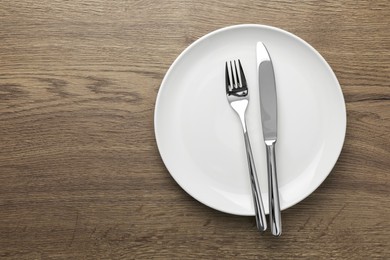 Photo of Plate, fork and knife on wooden table, top view. Space for text