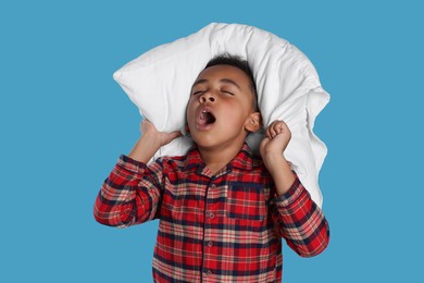Photo of Boy covering his ears with pillow and yawning on light blue background. Insomnia problem