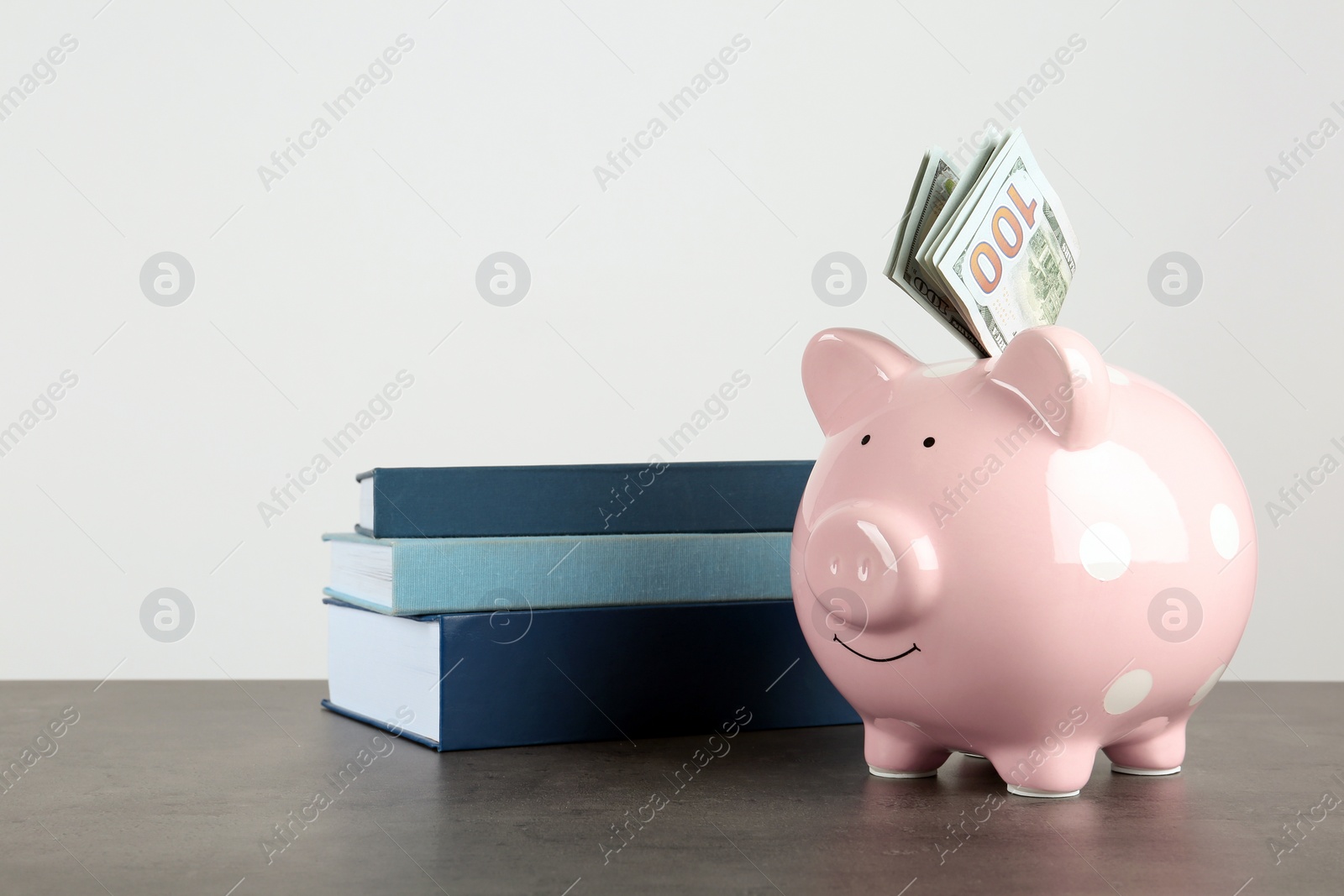 Photo of Piggy bank with dollars and books on table against white background