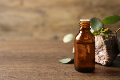 Photo of Bottle of eucalyptus essential oil, stone and leaves on wooden table. Space for text