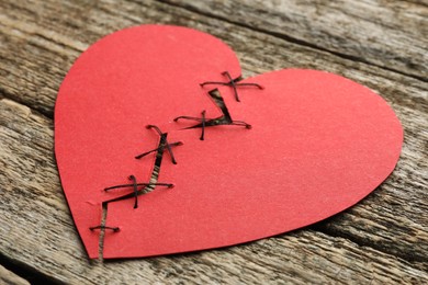 Photo of Broken heart. Torn red paper heart sewed with thread on wooden table, closeup