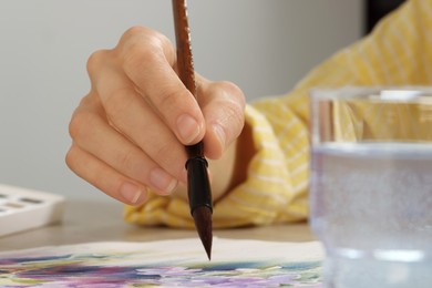 Woman painting flowers with watercolor at white wooden table, closeup. Creative artwork