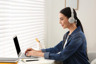Photo of Online translation course. Student in headphones typing on laptop at home