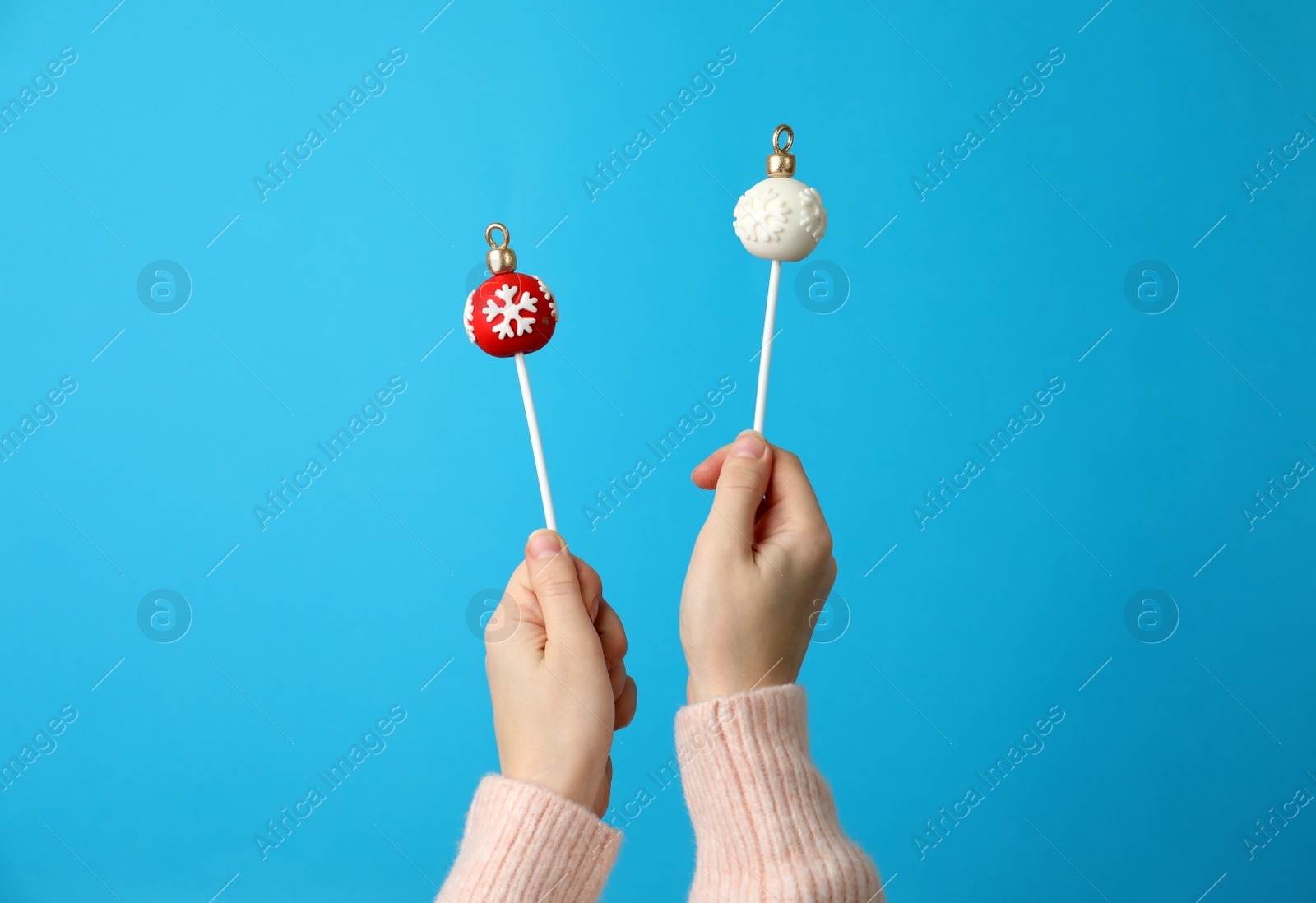 Photo of Woman holding delicious Christmas themed cake pops against light blue background, closeup