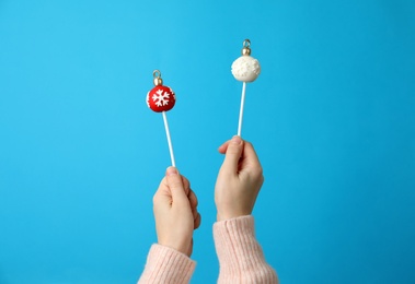 Photo of Woman holding delicious Christmas themed cake pops against light blue background, closeup