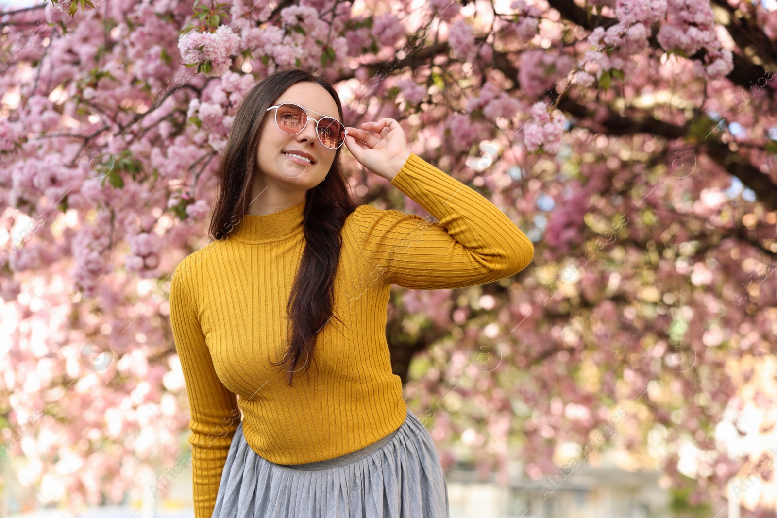 Photo of Beautiful woman in sunglasses near blossoming tree on spring day, space for text