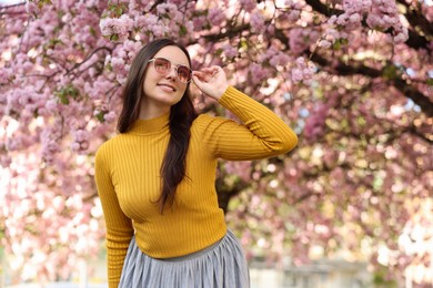 Beautiful woman in sunglasses near blossoming tree on spring day, space for text