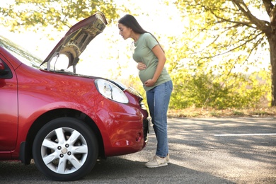 Stressed pregnant woman near broken car outdoors