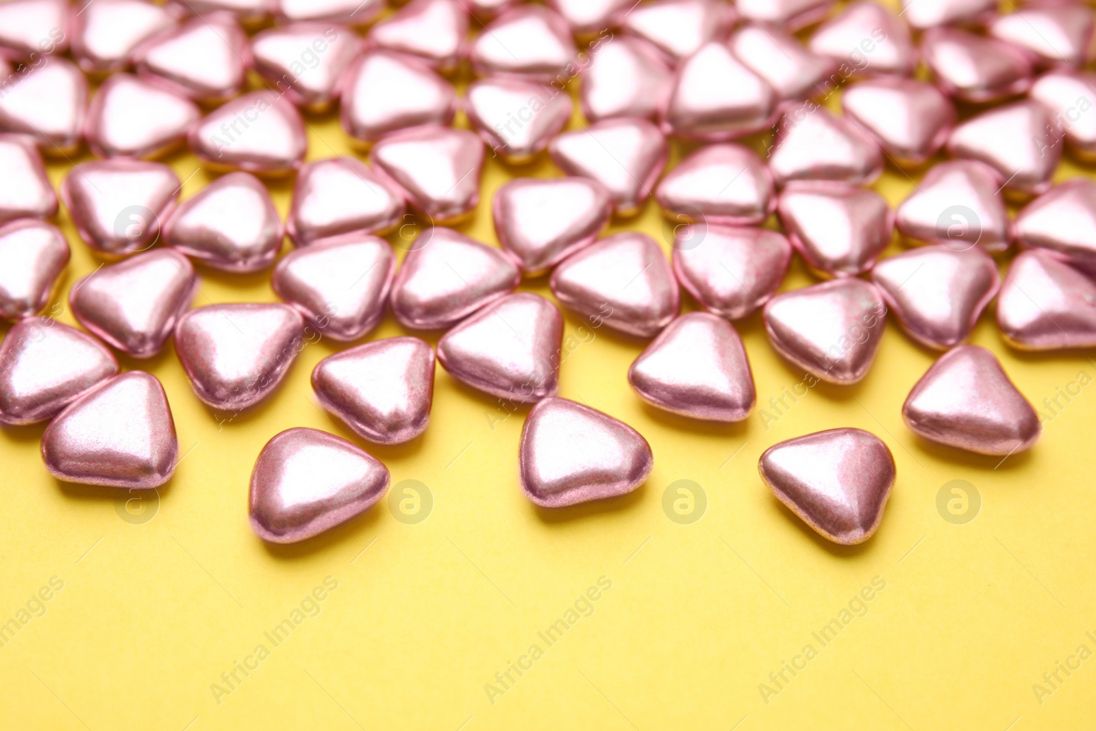 Photo of Many delicious heart shaped candies on yellow background