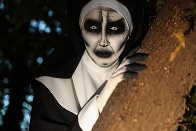 Photo of Scary devilish nun near tree outdoors. Halloween party look