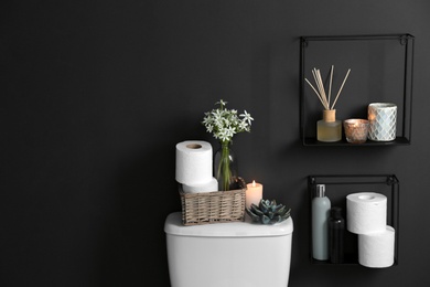 Photo of Decor elements, necessities and toilet bowl near black wall, space for text. Bathroom interior