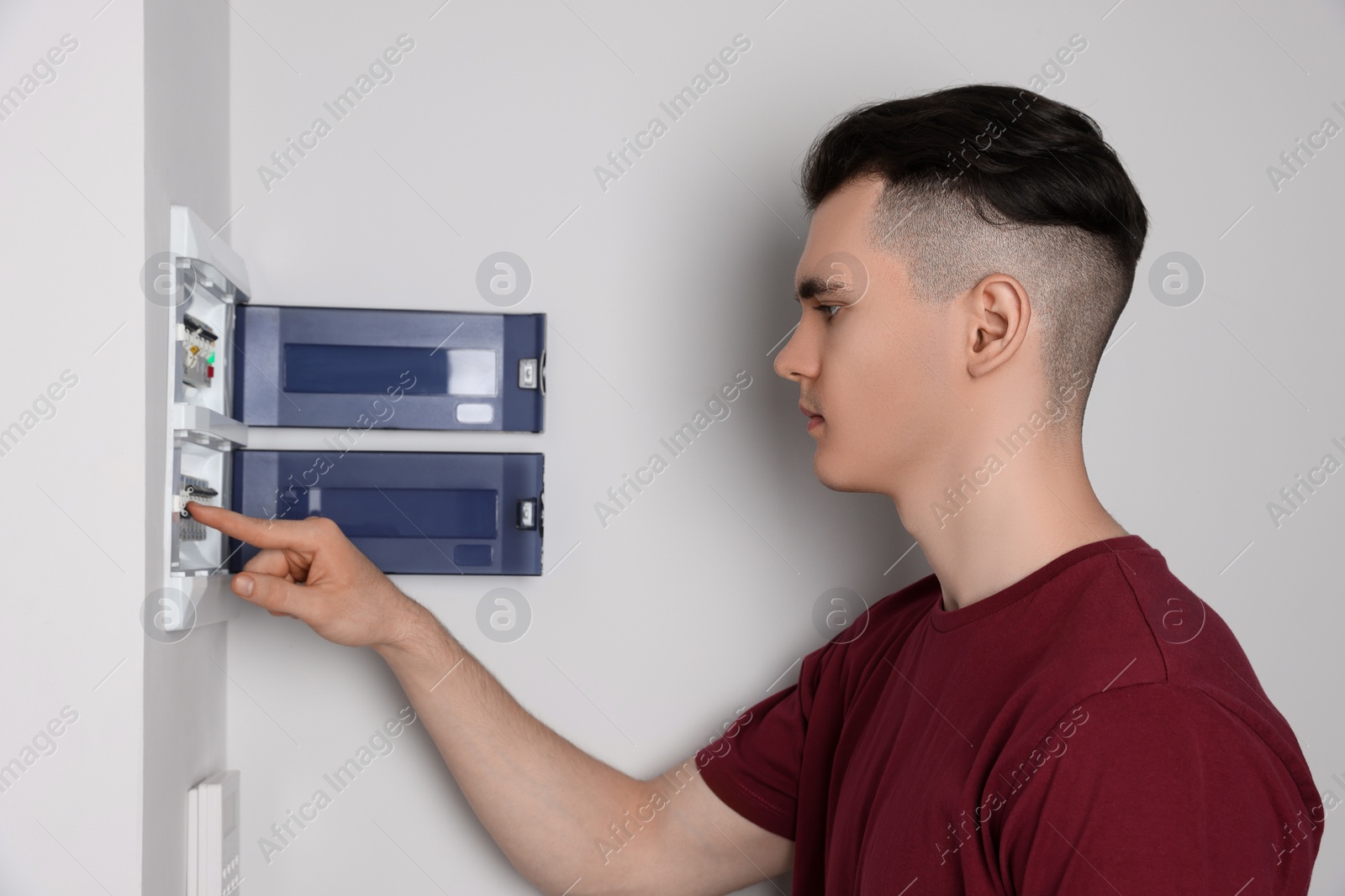 Photo of Young handyman pressing switch on electrical panel board indoors