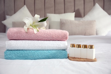 Stack of clean towels, flower and shampoo bottles on bed