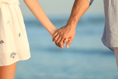 Photo of Happy young couple holding hands at beach on sunny day, closeup