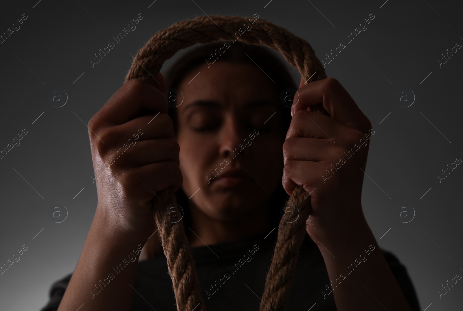 Photo of Depressed woman with rope noose on grey background, low angle view