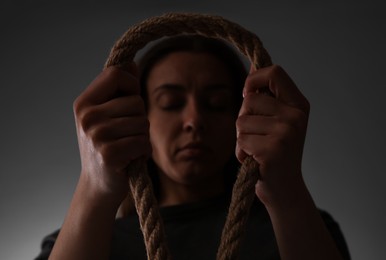 Photo of Depressed woman with rope noose on grey background, low angle view