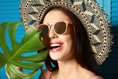Photo of Beautiful woman wearing sunglasses and hat with tropical leaf near blue wooden folding screen