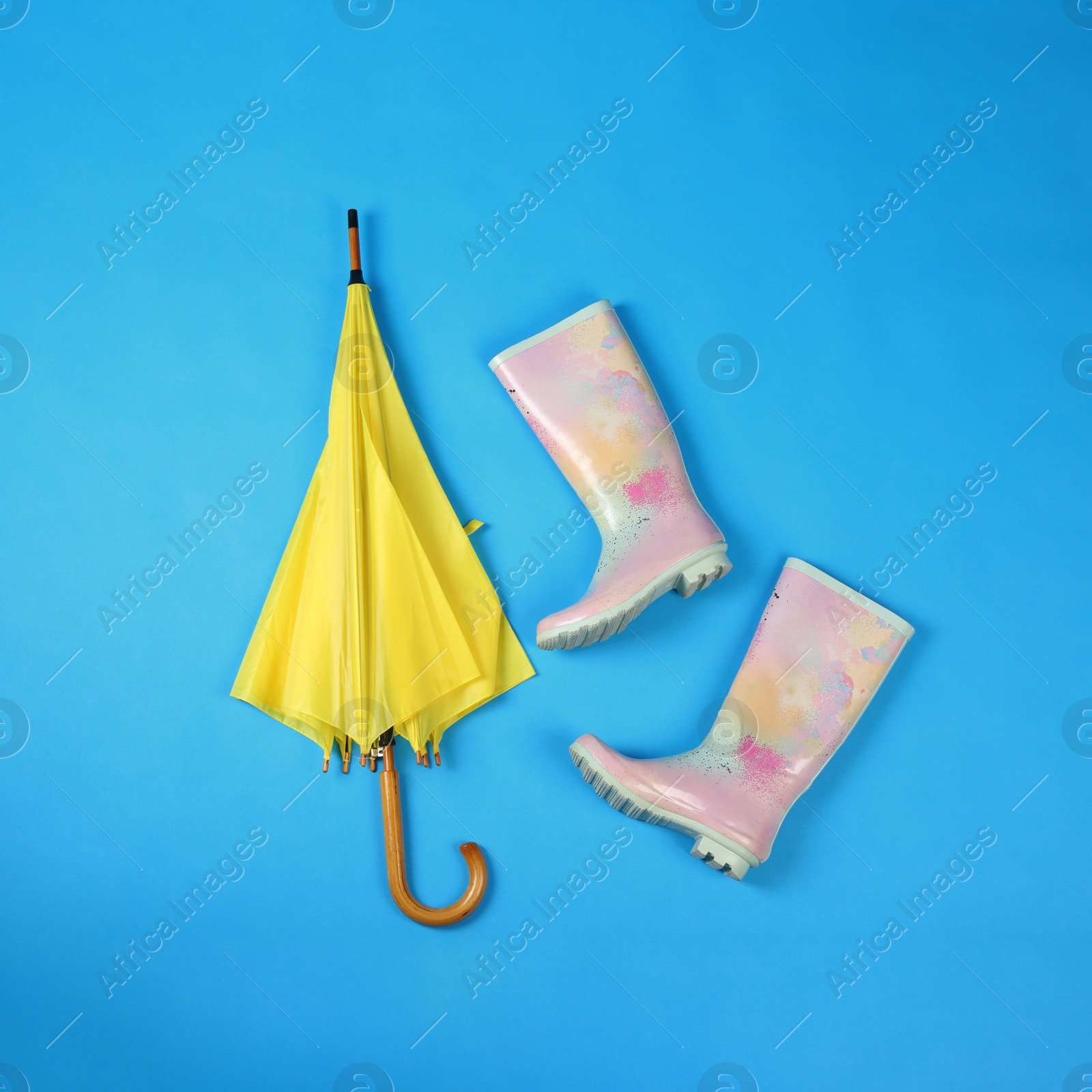 Photo of Beautiful yellow umbrella and rubber boots on blue background, flat lay