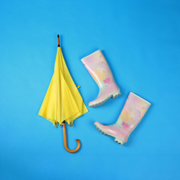 Photo of Beautiful yellow umbrella and rubber boots on blue background, flat lay