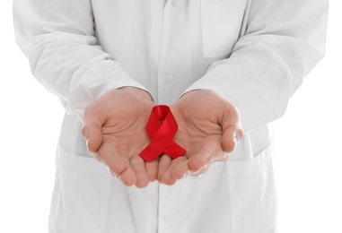 Doctor holding red awareness ribbon on white background, closeup. World AIDS disease day