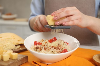 Photo of Woman grating cheese onto delicious pasta at table in kitchen, closeup