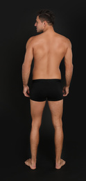 Man in underwear on black background, back view