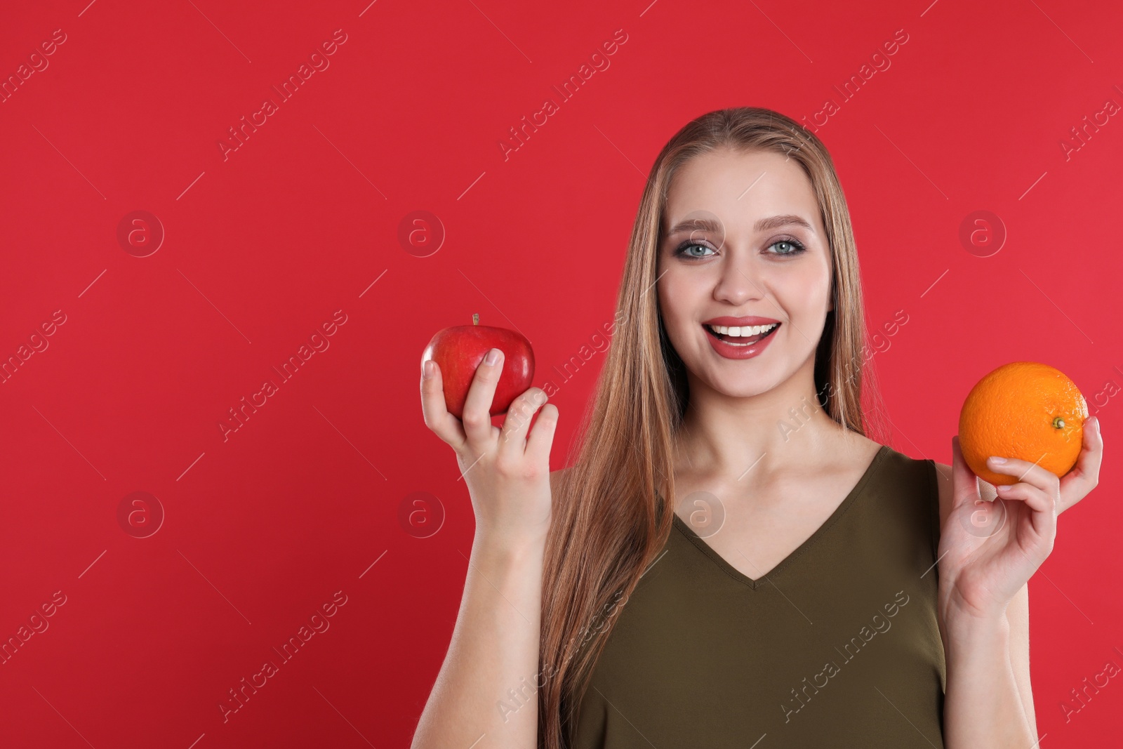 Photo of Young woman with apple and orange on red background, space for text. Vitamin rich food