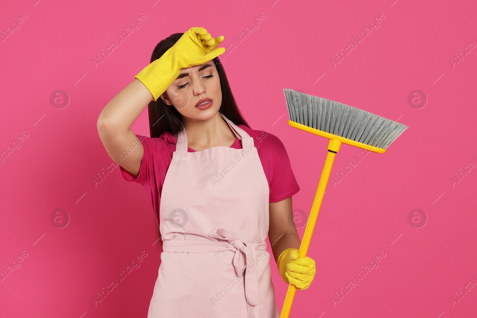 Photo of Tired young woman with broom on pink background