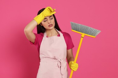 Tired young woman with broom on pink background